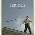 A man standing on the roof of a house, looking off to his left. His hands are on his hips. Behind him is a TV aerial.